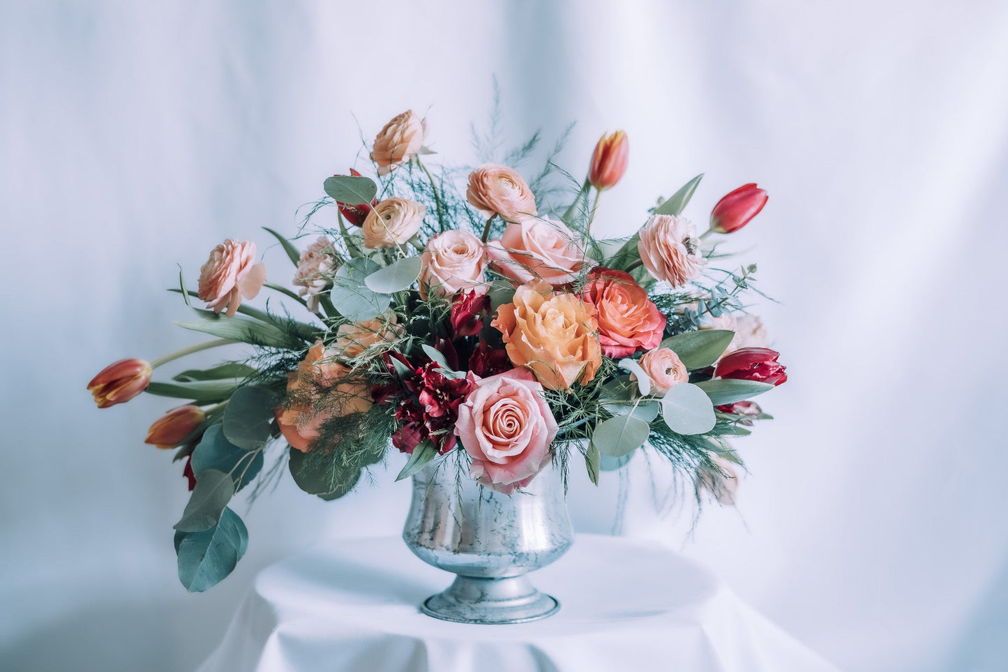 Floral arrangement in a silver vase on a white tablecloth with a white background